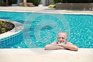 Happy elderly caucasian swimming in pool during retirement holiday with relaxation and smiling. Old man having good time in hotel