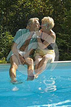 Felice coppia di anziani divertirsi mentre si è seduti sul bordo della piscina e prendere in giro a vicenda.
