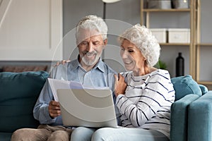 Happy elderly couple clients pay bills on laptop online