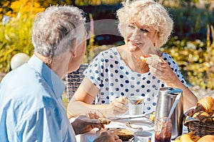 Happy elderly couple eating breakfast in their garden outdoors i