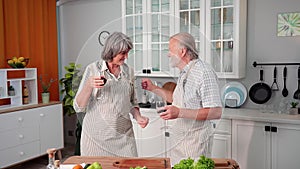 happy elderly couple have kept love for many years and are happy to prepare a snack with glasses of wine and dancing in