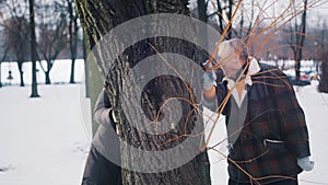 Happy elderly couple hiding behind the tree and kissing. Love and affection at old age. Valentines day