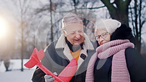Happy elderly couple hugging and playing with airplane toy in the park in winter.