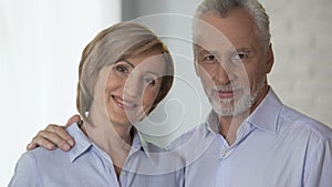 Happy elderly couple looking at each other and smiling at camera, advertising