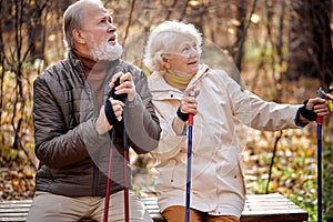Happy elderly couple in love engaged in Nordic walking in park, have rest
