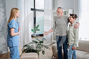 Happy elderly couple meeting medical nurse at home