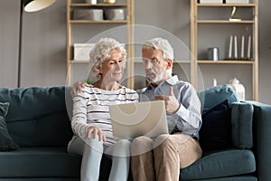 Happy elderly couple relax on couch using laptop