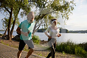 Happy elderly couple running on beach enjoying jogging workout in morning