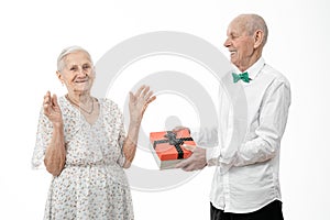 Happy elderly couple, senior man in white shirt present gift box to his old woman in white dress, celebrating birthday