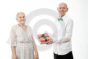 Happy elderly couple, senior man in white shirt present gift box to his old woman in white dress, celebrating birthday