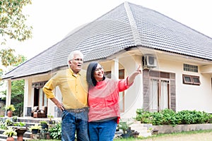 Happy elderly couple showing thumbs up in front of their new house