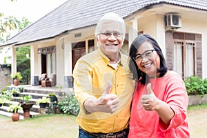 Happy elderly couple showing thumbs up in front of their new res