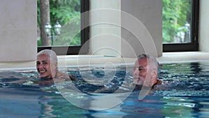 Happy elderly couple swimming in indoor hotel pool