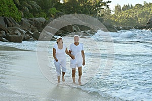 Happy elderly couple walking on tropical beach