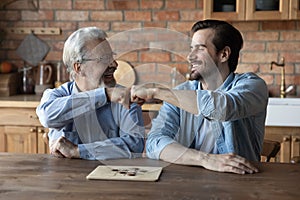 Happy elderly dad and grownup son giving fist bumps