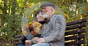 Happy elderly family spends leisure sitting on a bench in the fresh air of an autumn city park. The wife strokes her
