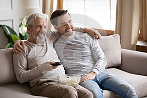Happy elderly father and adult son watch TV