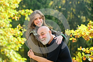 Happy elderly father and daughter enjoying tender autumn moment, smiling. Grown up daughter hugging mature man from back