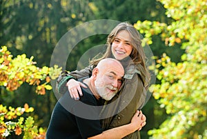 Happy elderly father and daughter enjoying tender autumn moment, smiling. Grown up daughter hugging mature man from back