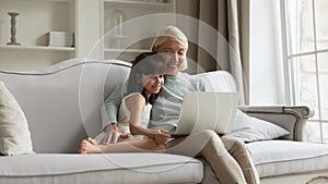 Elderly grandmother and little granddaughter relax using laptop photo