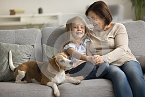Happy elderly grandmother and grandkid resting with dog on couch