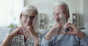 Happy elderly husband and wife making finger hearts