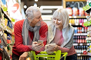 Happy elderly husband and wife shopping together, using smartphone photo