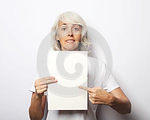 Happy elderly lady holding blank sheet in hand, smiling over white background