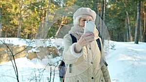 Happy elderly lady taking selfie with smartphone camera posing in park in winter