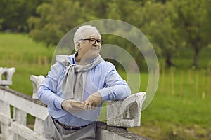 Happy elderly man with a book in his hands is resting in the park outdoors.