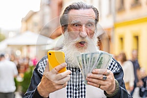 Happy elderly man counting money dollar cash, use smartphone calculator app in urban city street