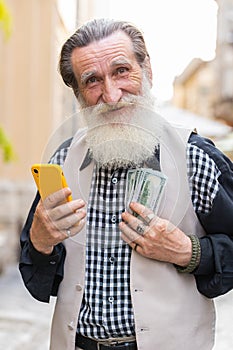 Happy elderly man counting money dollar cash, use smartphone calculator app in urban city street