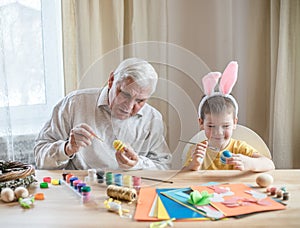 Happy elderly man granfather preparing for Easter with grandson. Portrait of smiling boy with bunny ears painted  colored eggs for