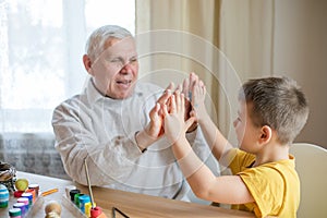 Happy elderly man granfather preparing for Easter with grandson. Portrait of smiling boy with bunny ears painted  colored eggs for