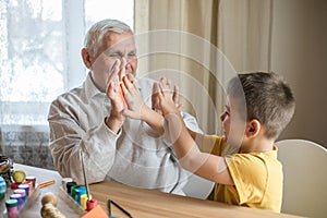 Happy elderly man granfather preparing for Easter with grandson. Portrait of smiling boy with bunny ears painted  colored eggs for