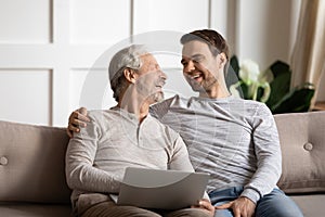 Happy elderly man holding computer enjoying fun time with son.