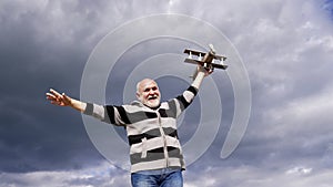 Happy elderly man pretend flying on model aircraft in sky, dream