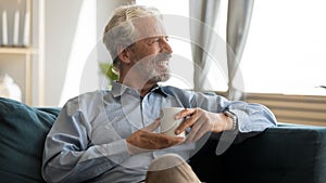 Happy elderly man resting on sofa with cup of tea.