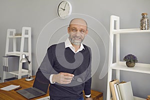 Happy elderly man smiling while standing at workplace at home indoors. Remote work learning online. Senior businessman