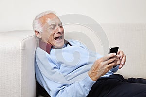 Happy elderly man using cell phone at home