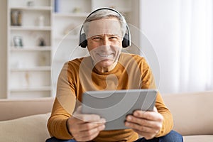 Happy elderly man using digital tablet and headphones at home