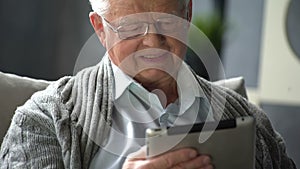 Happy elderly man is using tablet computer at home