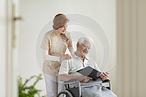 Happy elderly man in the wheelchair reading a book during visit
