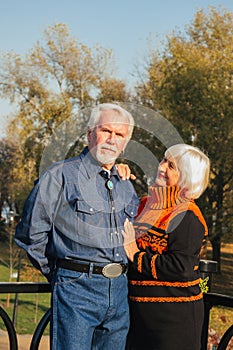 Happy elderly man and woman sitting on a bench in autumn day. Relaxed senior couple sitting on a park bench. Grandfather gently