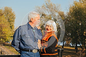 Happy elderly man and woman sitting on a bench in autumn day. Relaxed senior couple sitting on a park bench. Grandfather gently