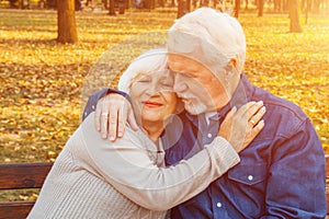 Happy elderly man and woman sitting on a bench in autumn day. Relaxed senior couple sitting on a park bench. Grandfather gently