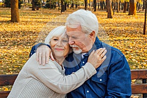 Happy elderly man and woman sitting on a bench in autumn day. Relaxed senior couple sitting on a park bench. Grandfather gently