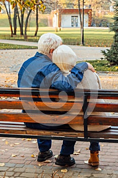 Happy elderly man and woman sitting on a bench in autumn day. Relaxed senior couple sitting on a park bench. Grandfather gently