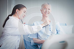 Happy Elderly patient talk with woman doctor at room in hospital. Doctor use stethoscope listening lung of elderly patient.