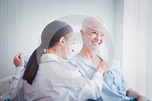 Happy Elderly patient talk with woman doctor at room in hospital. Doctor use stethoscope listening lung of elderly patient.